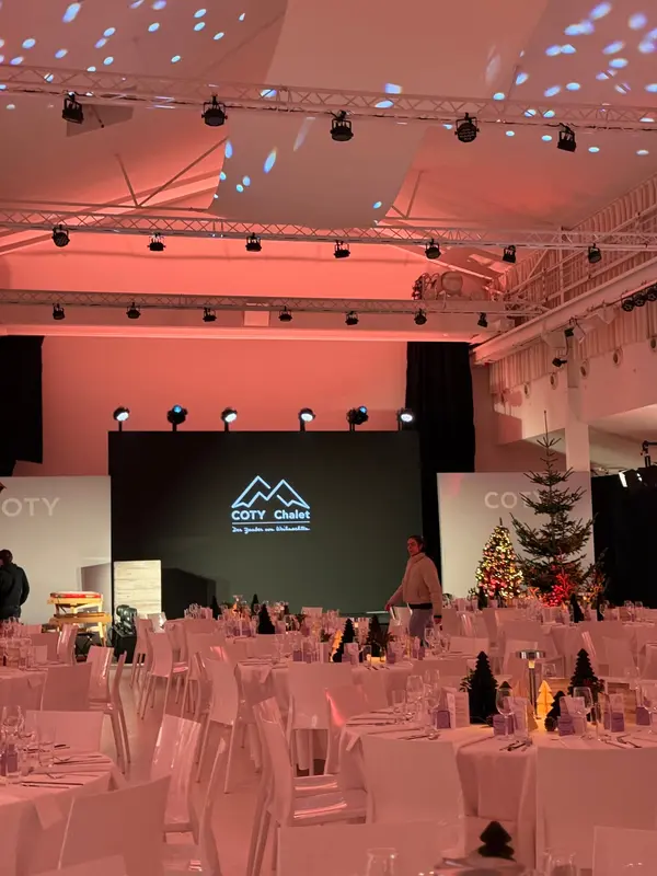 Weihnachtsfeier einer Firma im B2LOFT: runde Tafeln vor der Bühne mit LED-Wand und Tannenbäumen