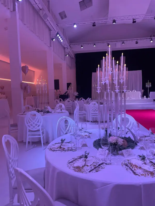 Festlich gedeckte runde Tafel mit gläsernem Kandelaber in rosé-violettem Licht